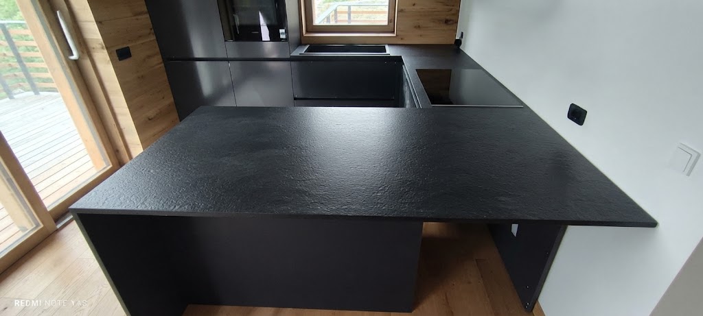 Cucina moderna con penisola nera opaca e dettagli in legno all'interno di un'abitazione luminosa.